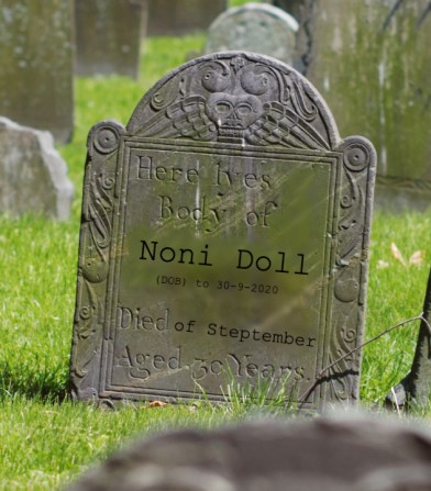 An old grave in a green cemetery. Poorly photoshopped on are the words: "Here lyes [sic] the body of Noni Doll. DOB to 30-9-2020. Died of Steptember. Aged 30 years."